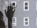 A black and white image of a hand held up against a window