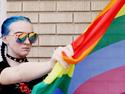 A person with blue hair holding up an LGBTQ+ flag