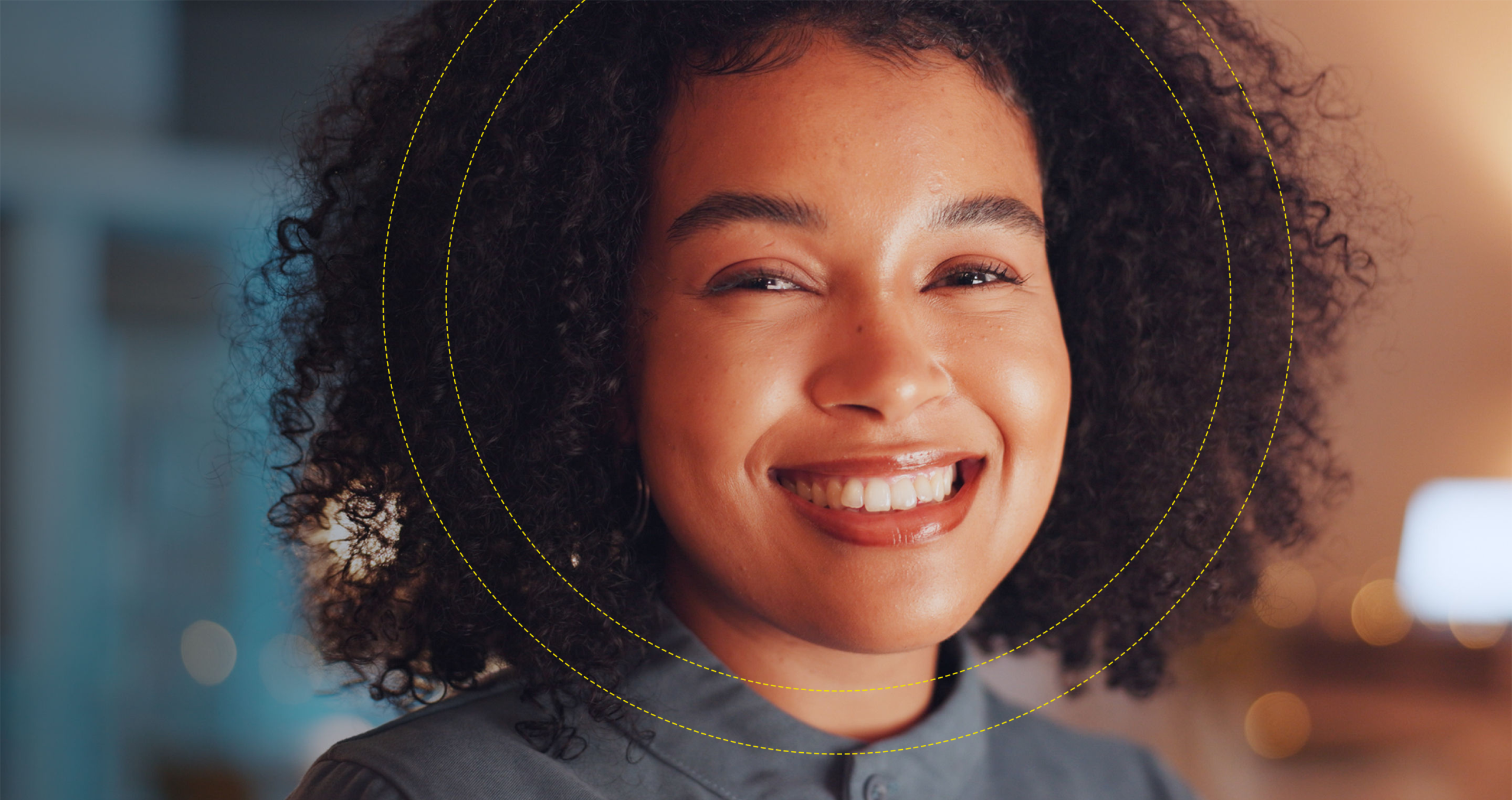 A close-up headshot of a woman with curly hair smiling directly at the camera